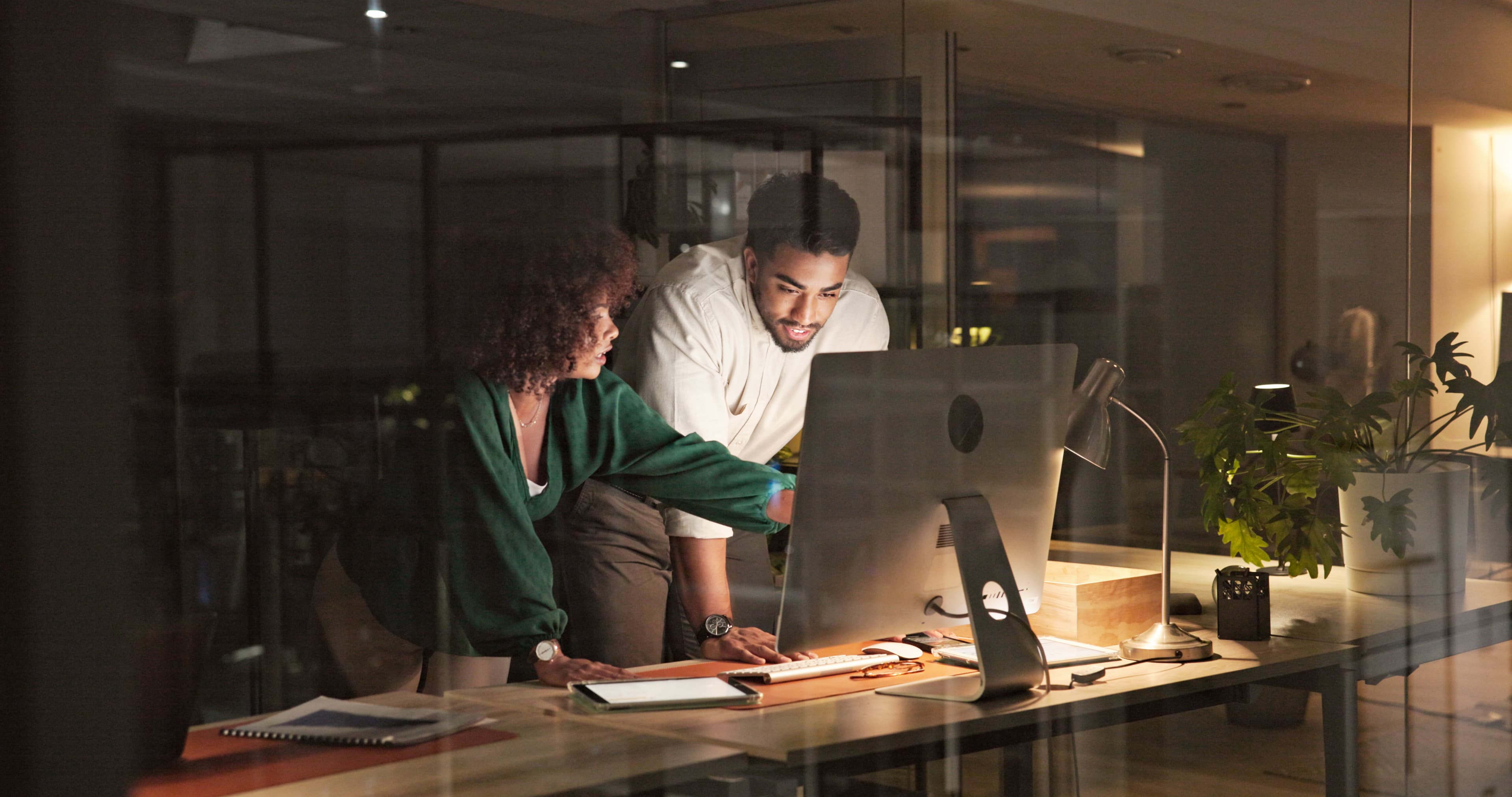 Two professionals collaborating at a desk in a modern office at night